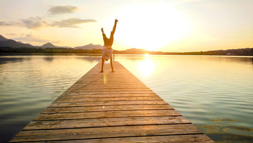 Woman doing handstand on pier over lake during sunset