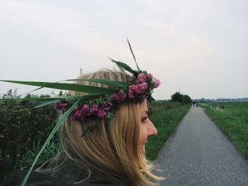 Young woman wearing tiara standing on road amidst grassy field against sky