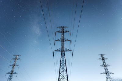 High voltage electricity pylon and transmission power line with milky way, blue tone.