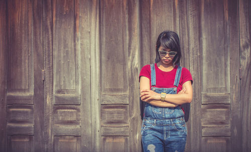 Woman with sunglasses standing against wall during sunny day