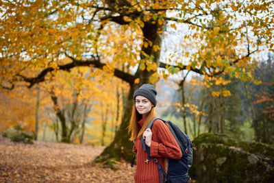 Portrait of young woman standing by trees during autumn