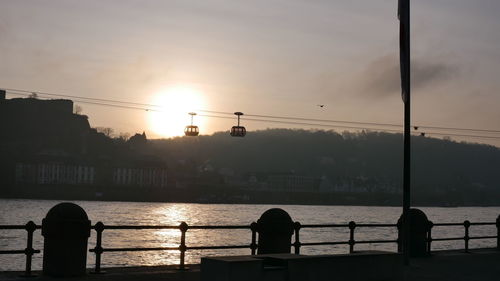 Silhouette city by river against sky during sunset