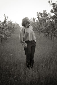 Rear view of young woman standing on field against sky