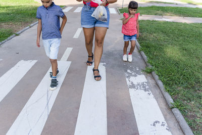 Two kids walking with their mother outdoors in a pathway in a park.