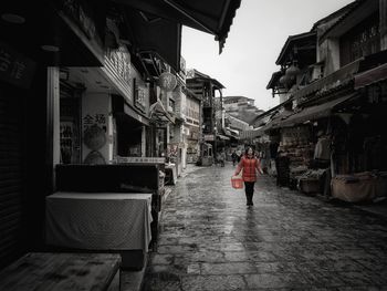 Rear view of woman walking on street amidst buildings