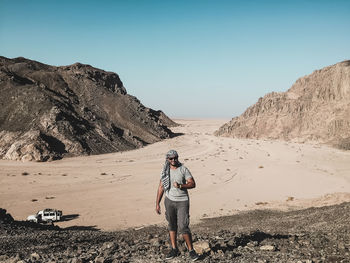 Full length of man standing on cliff against mountains at desert