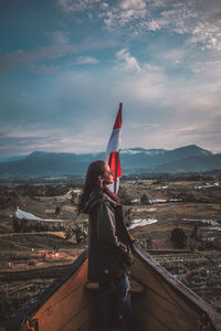 Woman standing on mountain by city against sky