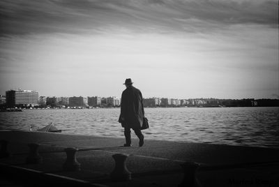 Rear view of man walking by sea against sky