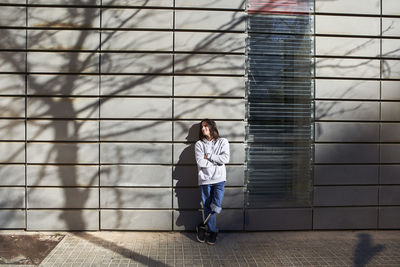 Disabled man with arms crossed standing against wall with tree shadow