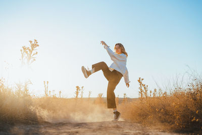 Full length of young woman jumping on field against clear sky