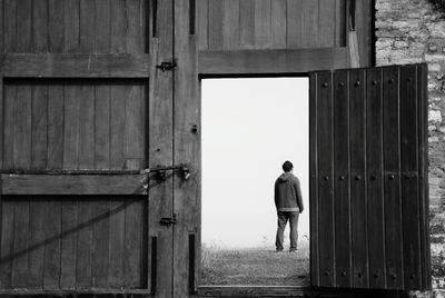 Rear view of man standing on field seen through open door