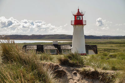 Lighthouse on field by building against sky