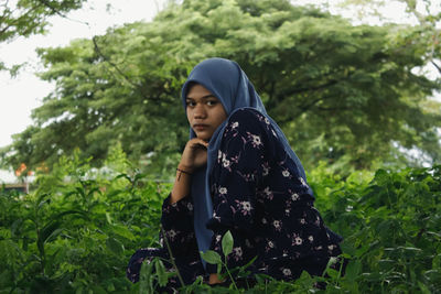 Young woman looking away while standing against plants