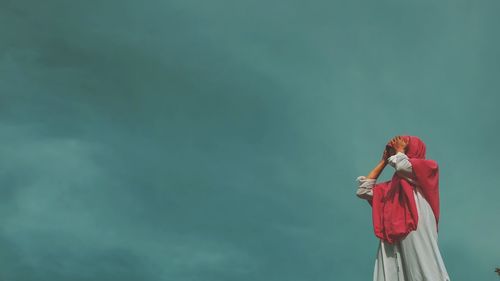 Woman with red umbrella standing against sky