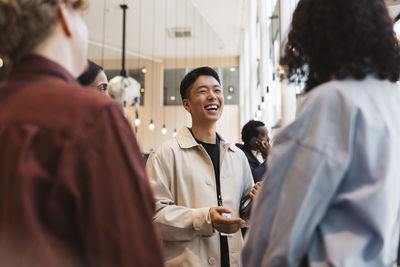Happy young male entrepreneur laughing while discussing strategies with delegates during seminar at convention center