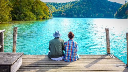 Rear view of couple sitting on jetty over lake