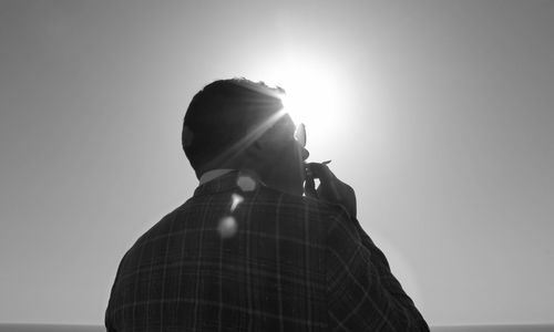 Rear view of man smoking cigarette against clear sky during sunny day