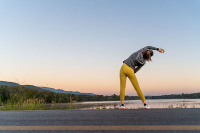 Back view of a woman stretching her arms and legs before her morning exercise at a local lake park
