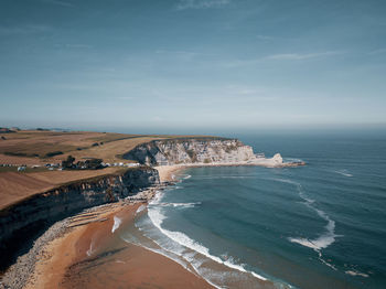 High angle view of beach and cliffs against sky with surfers in the water