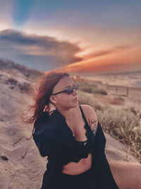 Young woman wearing sunglasses standing on beach during sunset