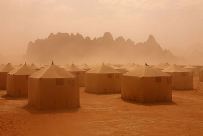 Tents with numbers in desert during sandstorm against sky