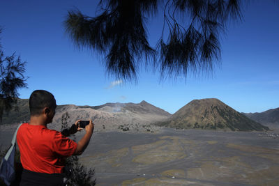 Rear view of man on mountain against clear blue sky