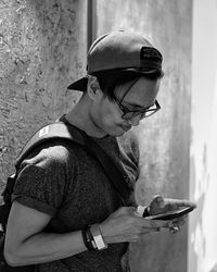 Fashionable man using mobile phone while standing by wall