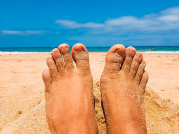 Low section of person at beach against blue sky