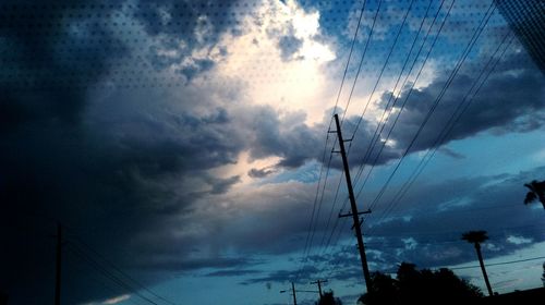 Low angle view of electricity pylon against cloudy sky