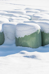 Snow covered haylage bales wrapped in green foil will provide food for farm animals during winter