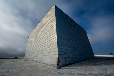 Side view of woman standing at oslo opera house against cloudy sky