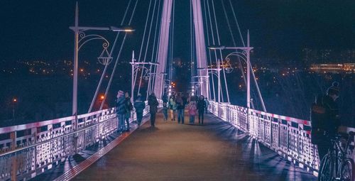 People on illuminated bridge in city against sky at night