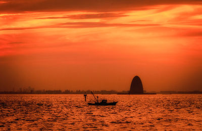 Silhouette boat sailing in sea against orange sky