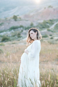 Pregnant woman holding belly standing on field