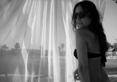 Sensuous woman wearing sunglasses by curtain