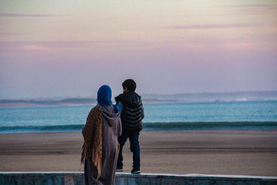 Rear view of couple on beach against sky