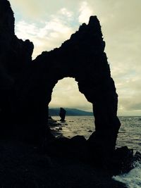 Silhouette rock formation on beach against sky during sunset