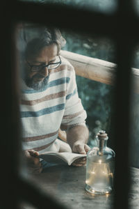 Man reading book seen through window