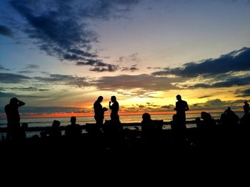 Silhouette people on beach against sky during sunset