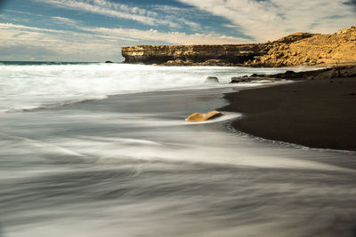 Scenic view retracting waves on dark beach against sky, fuerteventura 