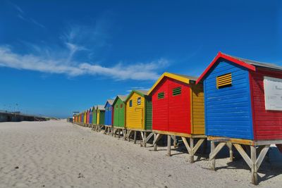 Colorful beach huts in row at beach against blue sky