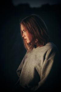 Woman looking away while standing against black background