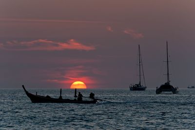 Sunset and sailboats silhouette, with thai longtail boat silhouette on foreground