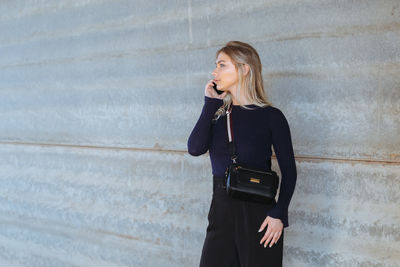 Young woman using mobile phone while standing against wall