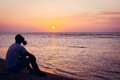 Man in gas mask relaxing at beach during sunset