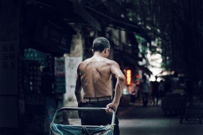 Rear view of shirtless man standing on street in city