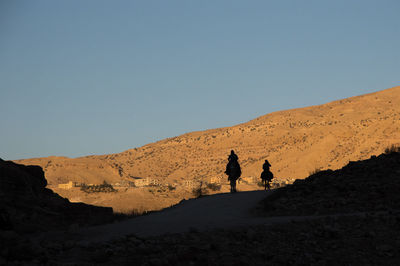 People riding camel on desert against clear sky