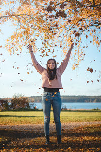 Candid portrait of 22 year old girl in pink sweatshirt and jeans throwing leaves.