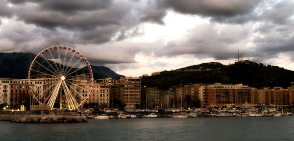 Ferris wheel in city against cloudy sky