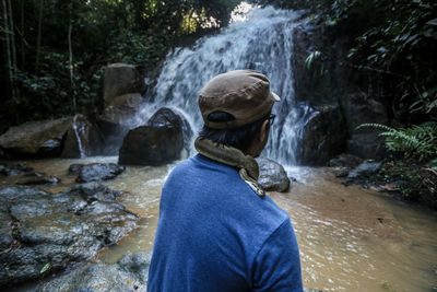 Rear view of woman standing by waterfall in forest